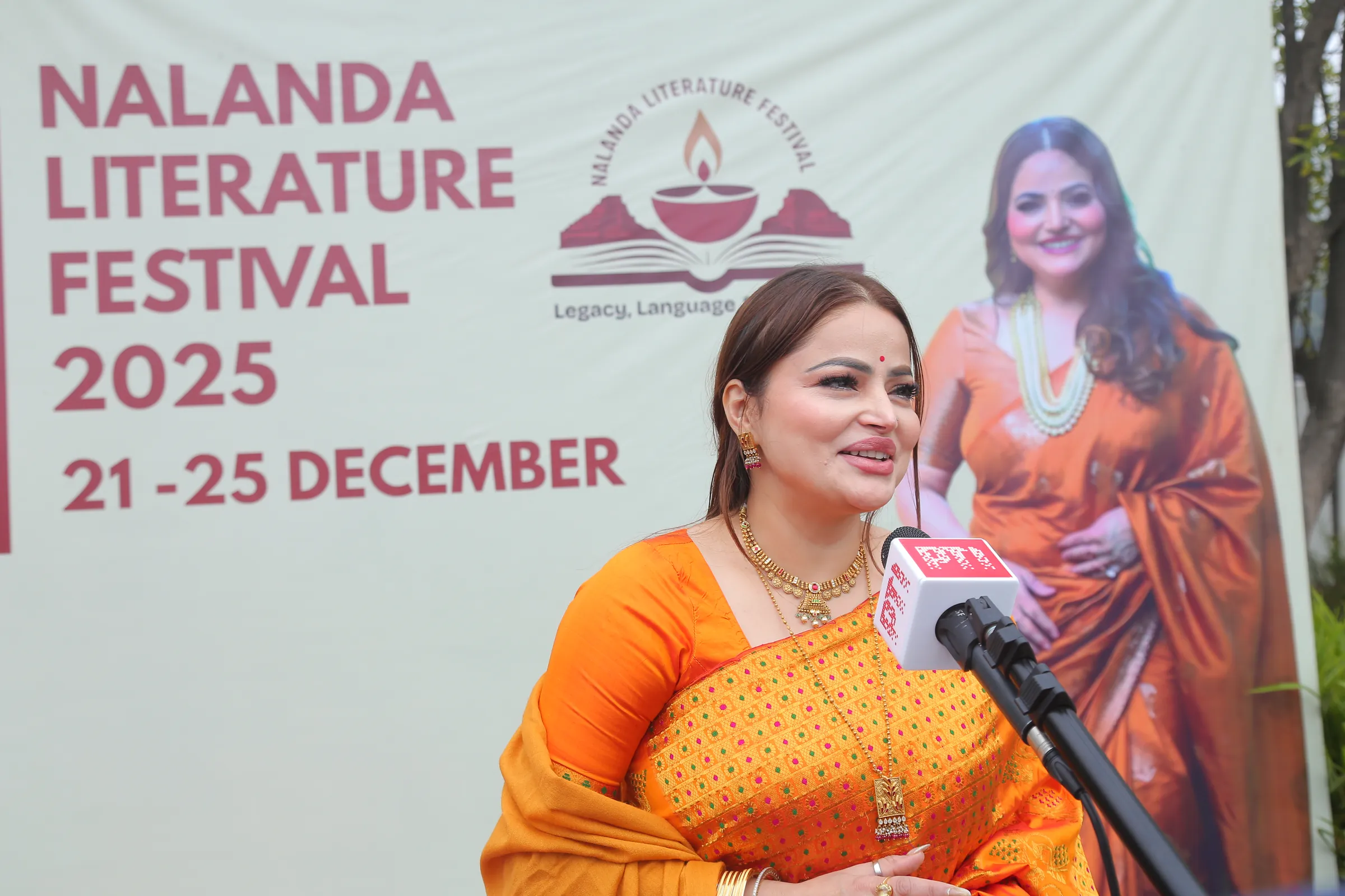 Ms. D. Aaliya speaking to the press in front of the Nalanda Literature Festival 2025 banner